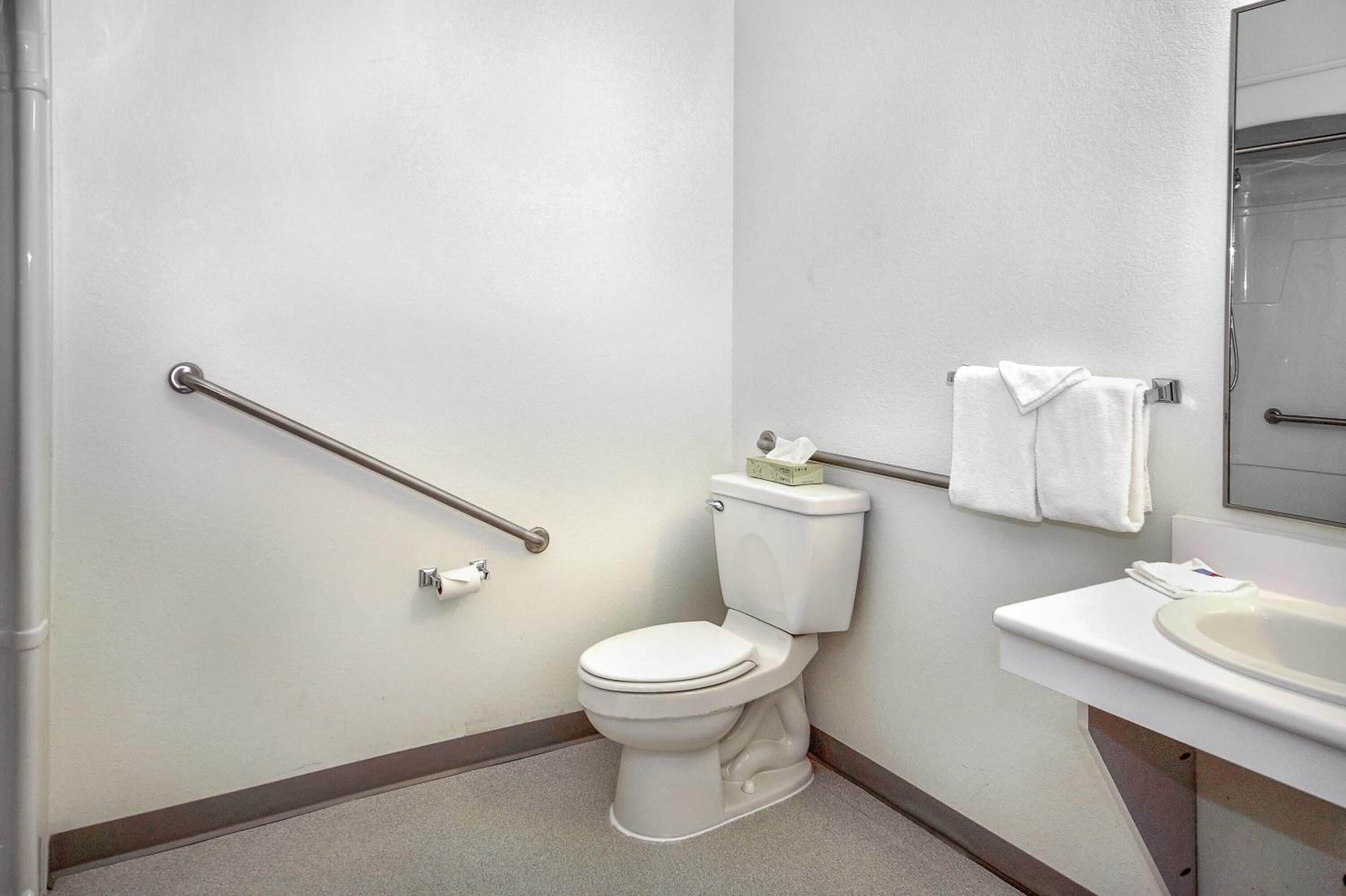 Une salle de bain standard équipée d’un WC, d’une barre d’appui, d’un lavabo et d’un porte-serviettes.