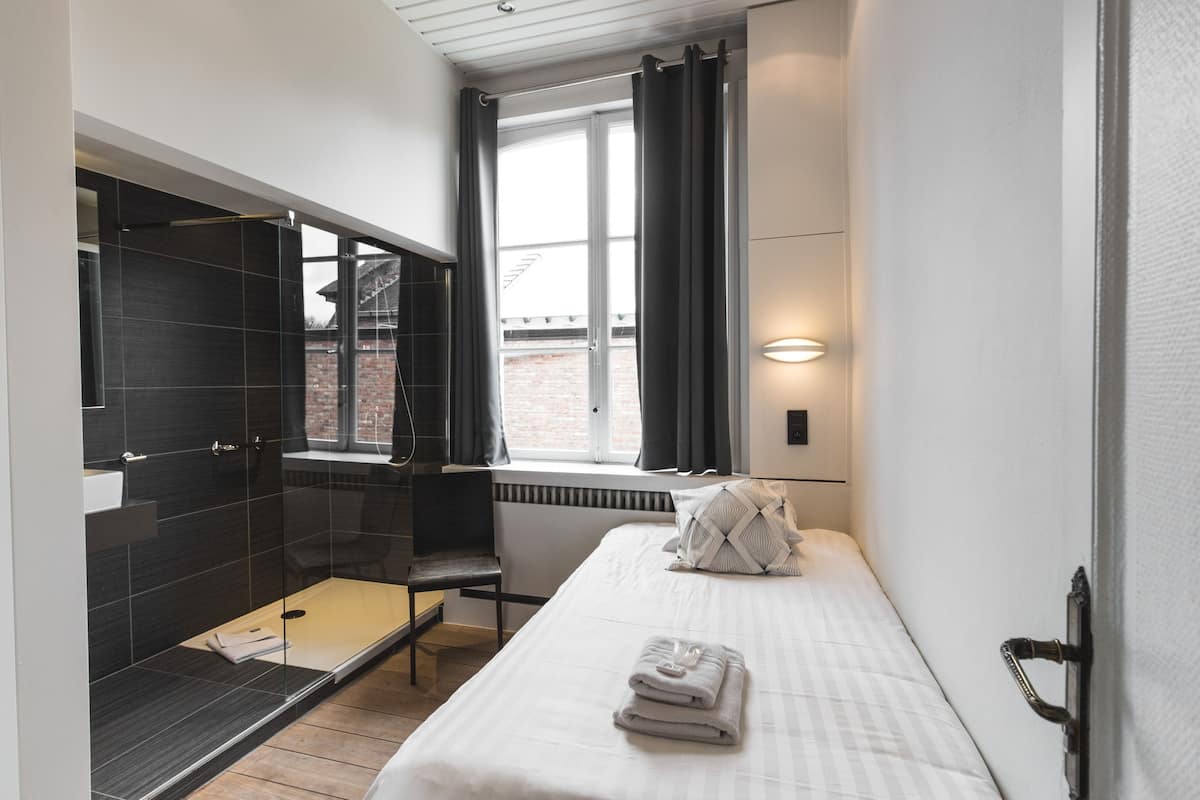 Une chambre d’hôtel moderne avec un grand lit, un espace douche et une fenêtre avec des rideaux.