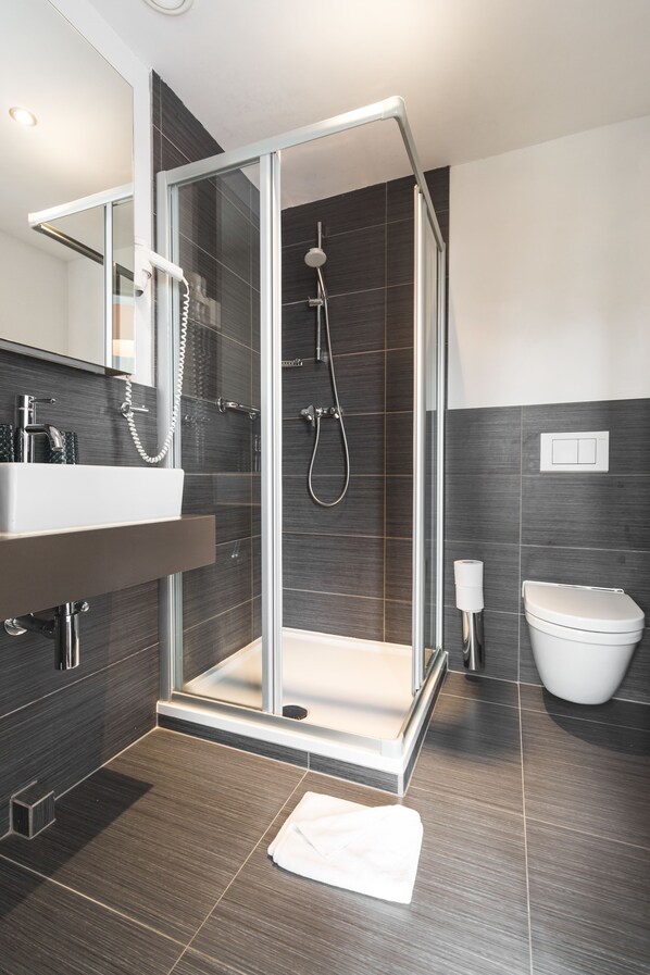 A modern bathroom with a glass-enclosed shower, a white sink, and a toilet. - Hotel de Goezeput (Bruges)