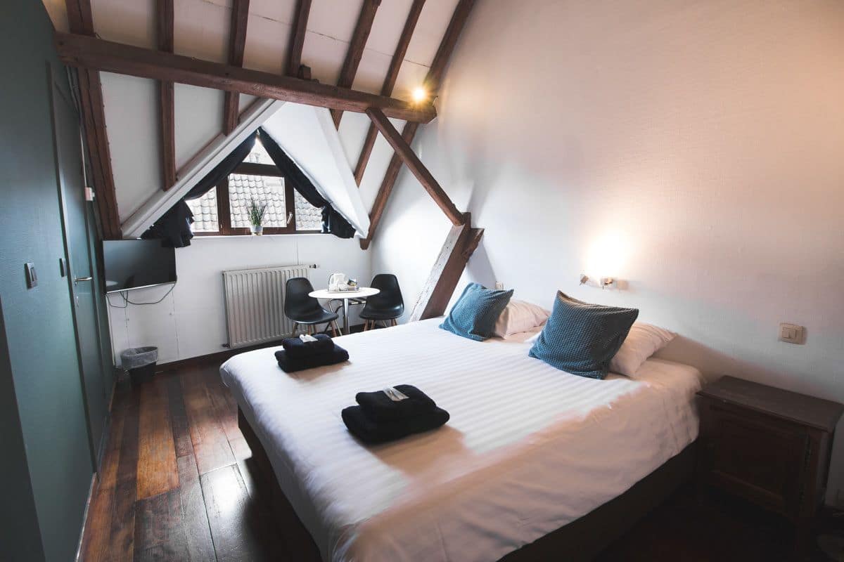 Une chambre avec un plafond en pente, un lit avec des oreillers, une petite table et une chaise.