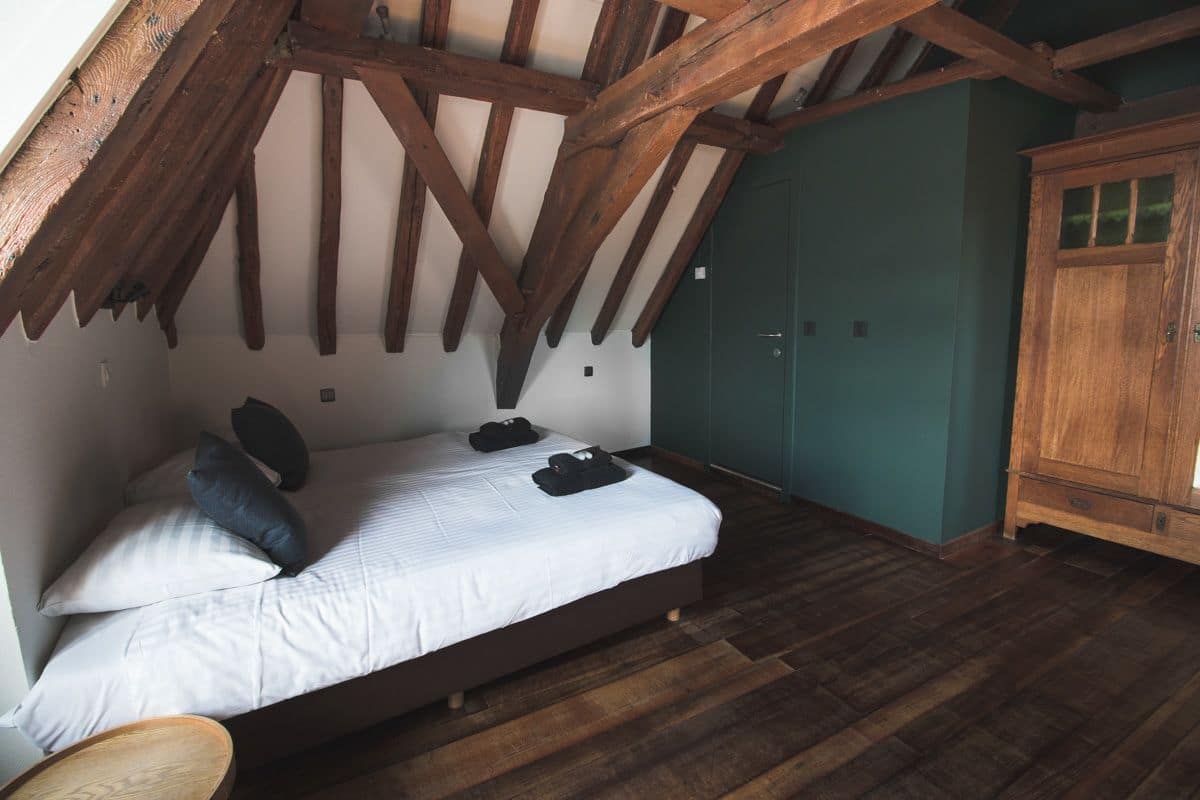 Une chambre avec un plafond en pente, des poutres en bois, un lit avec des oreillers, une armoire en bois et un mur vert.