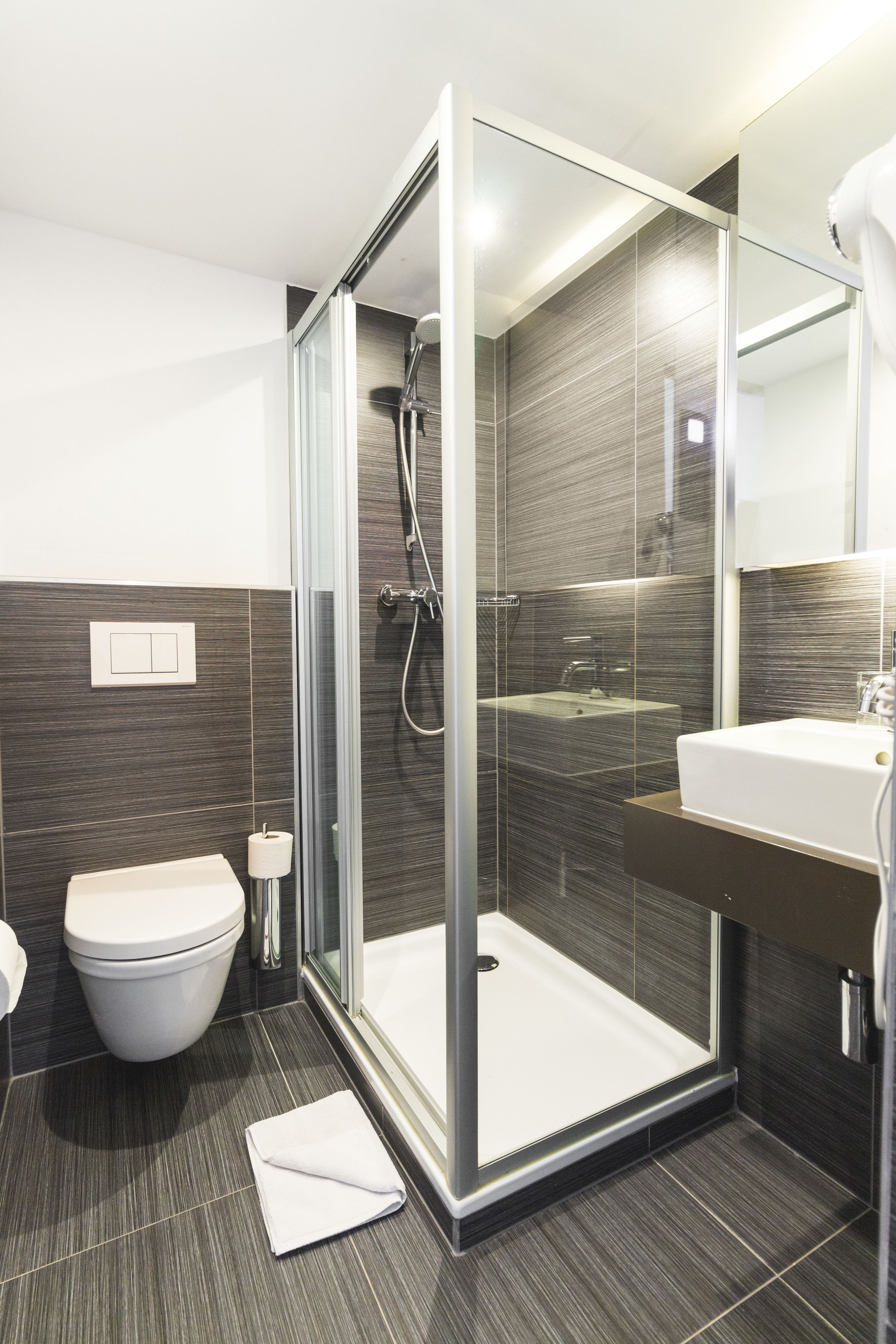 Un baño moderno con ducha compartimentada por vidrio, inodoro blanco y lavamanos con espejo.