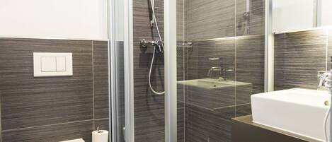 Un baño moderno con ducha compartimentada por vidrio, inodoro blanco y lavamanos con espejo.