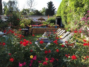 Un jardin avec des roses rouges, un mur de pierre et un bâtiment avec un toit en tuiles.