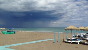 Une plage avec des transats et des parasols, un ciel dégagé et une mer calme.