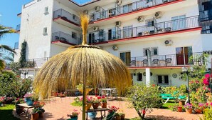 Un hôtel à plusieurs étages doté de balcons, de sièges en plein air et d’un parasol en chaume.