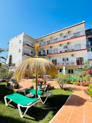 A multi-story hotel with balconies, outdoor seating, and a thatched umbrella. - Hotel Carmen Teresa (Torremolinos)
