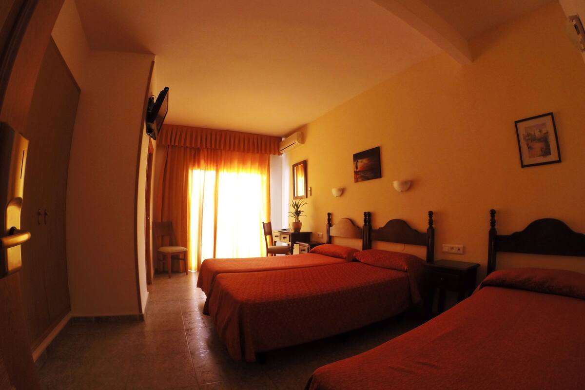 A hotel room with two beds, a desk, a chair, and a window with curtains.