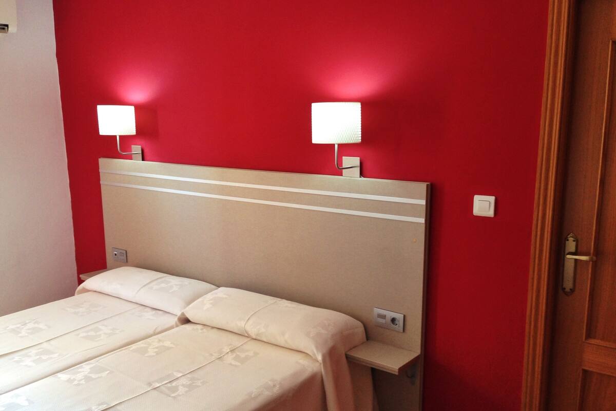 A hotel room with a bed, two bedside lamps, and a wooden door.