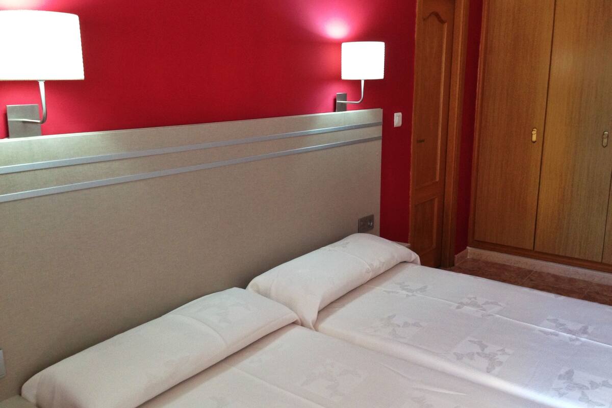 A hotel room with a bed, two bedside lamps, and a wooden wardrobe.