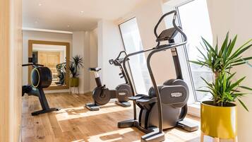 A modern home gym with cardio and strength equipment, large windows, and indoor plants.
