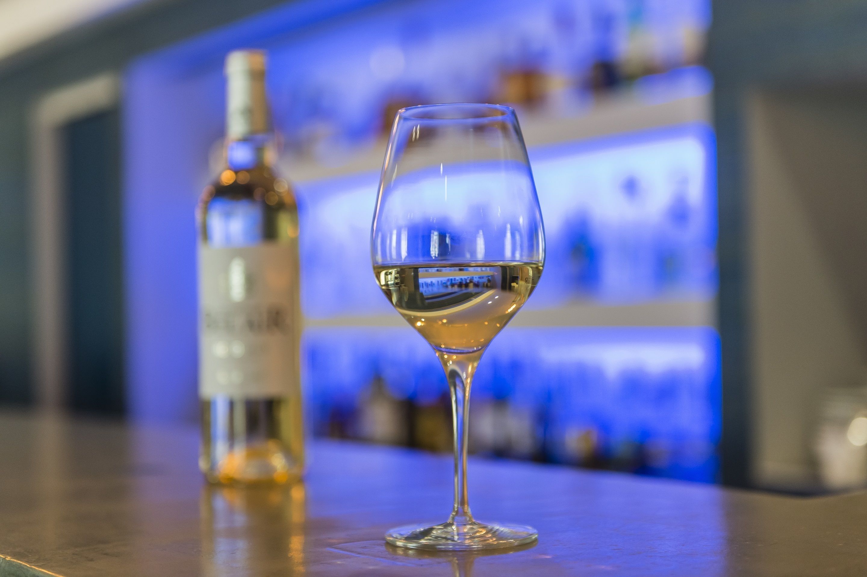 Una copa de vino blanco y una botella sobre una barra.