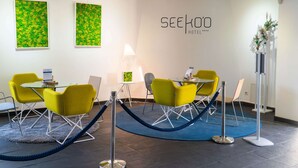 Un hall d’hôtel avec des chaises jaunes, une table en verre et une barrière faite d’une corde bleue.