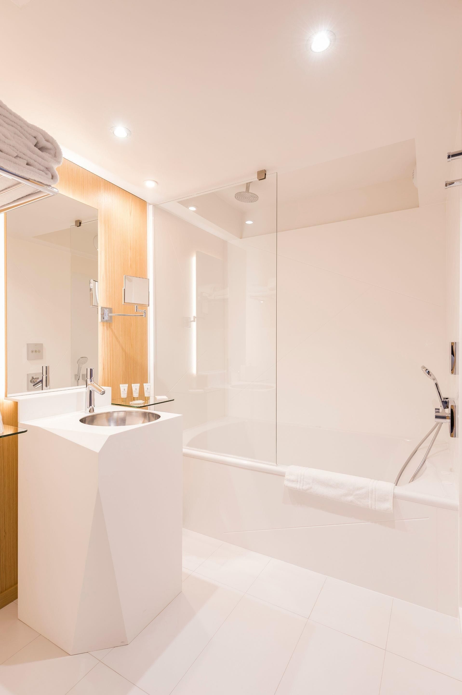 Un baño moderno con cabina de ducha de vidrio, un lavabo blanco con espejo y un mueble de tocador de madera.
