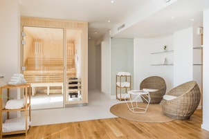 A modern bathroom with a wooden bench, a glass shower enclosure, and a small round table with a magazine.