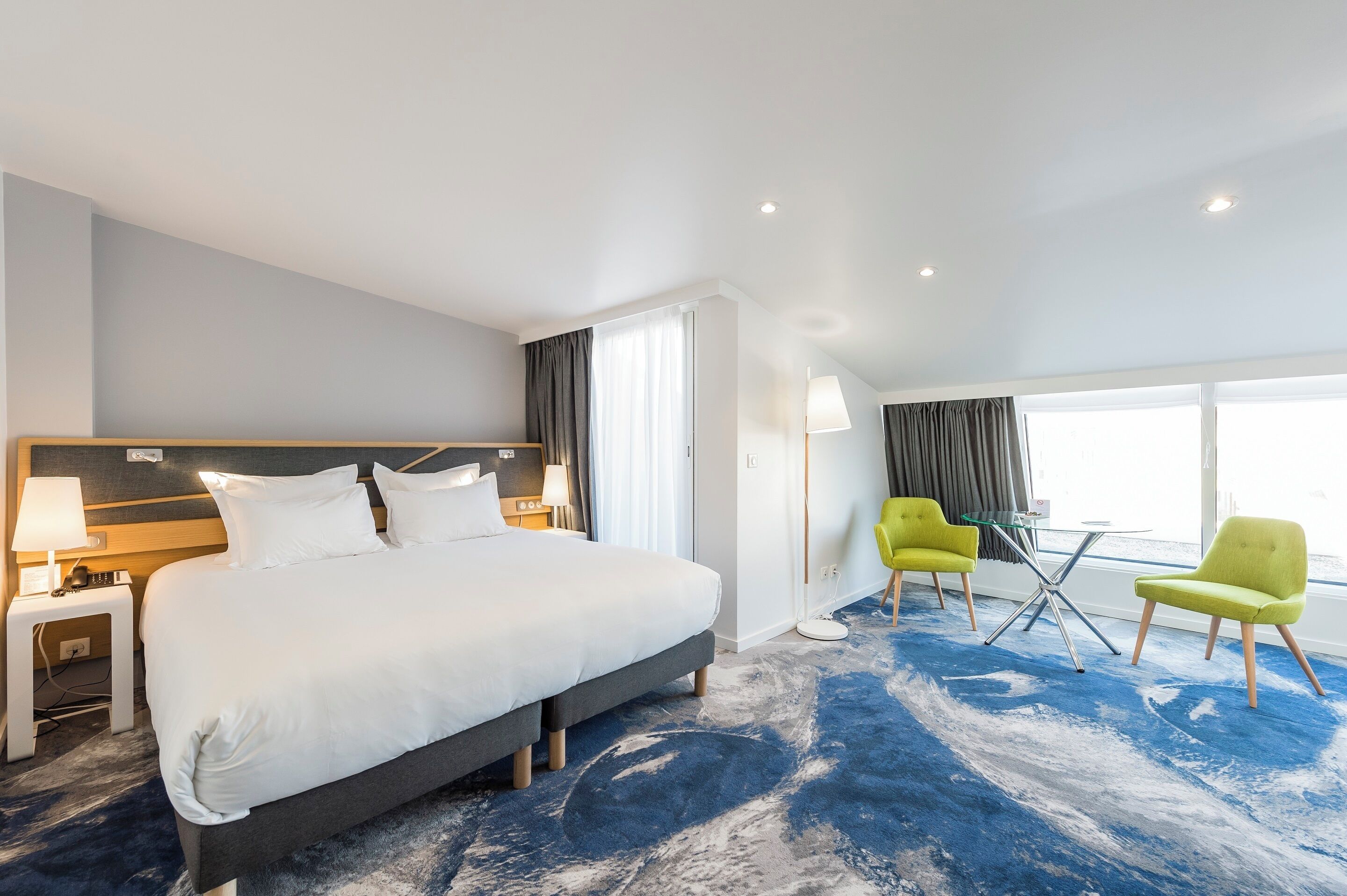 A hotel room with a large bed, two chairs, a table, and a window with curtains.