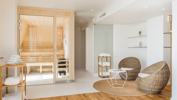 Une chambre moderne avec un banc en bois, des chaises en osier, une petite table et des étagères contenant des serviettes.