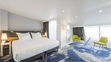 Una habitación de hotel moderna con una cama grande, dos sillas, una mesita y una ventana con cortinas.