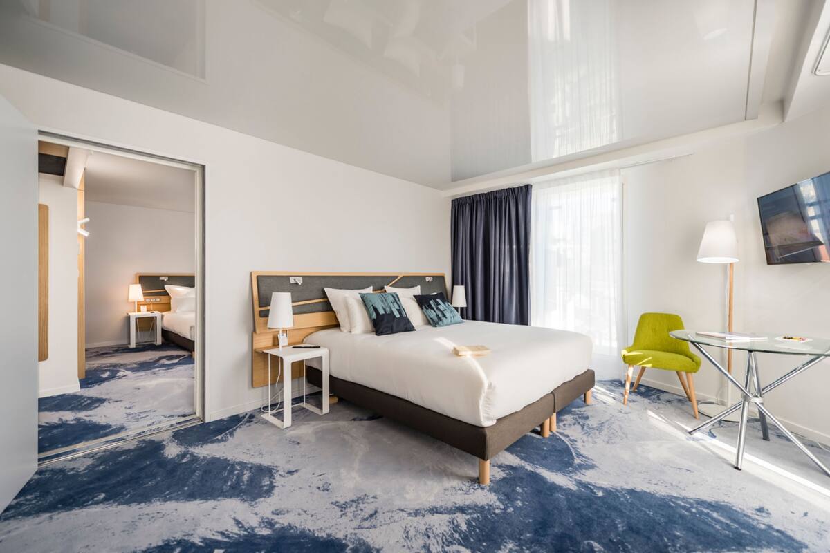 Una habitación de hotel moderna con una cama grande, un escritorio, una silla y un televisor en la pared.