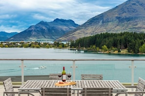 A wooden table with a bottle of wine and glasses, overlooking a lake with mountains in the background. - Oaks Queenstown Club Suites (Queenstown)