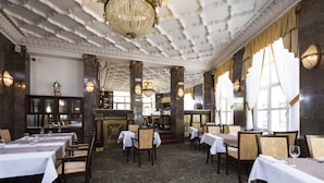 A formal dining area with tables set for service, ornate ceiling, and classic lighting fixtures.
