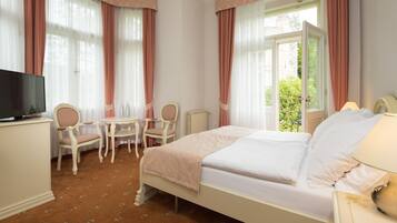 A hotel room with a bed, a desk, two chairs, a television, and a window with curtains.