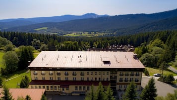 Ein mehrstöckiges Gebäude mit flachem Dach, umgeben von Grünflächen und Bergen im Hintergrund.