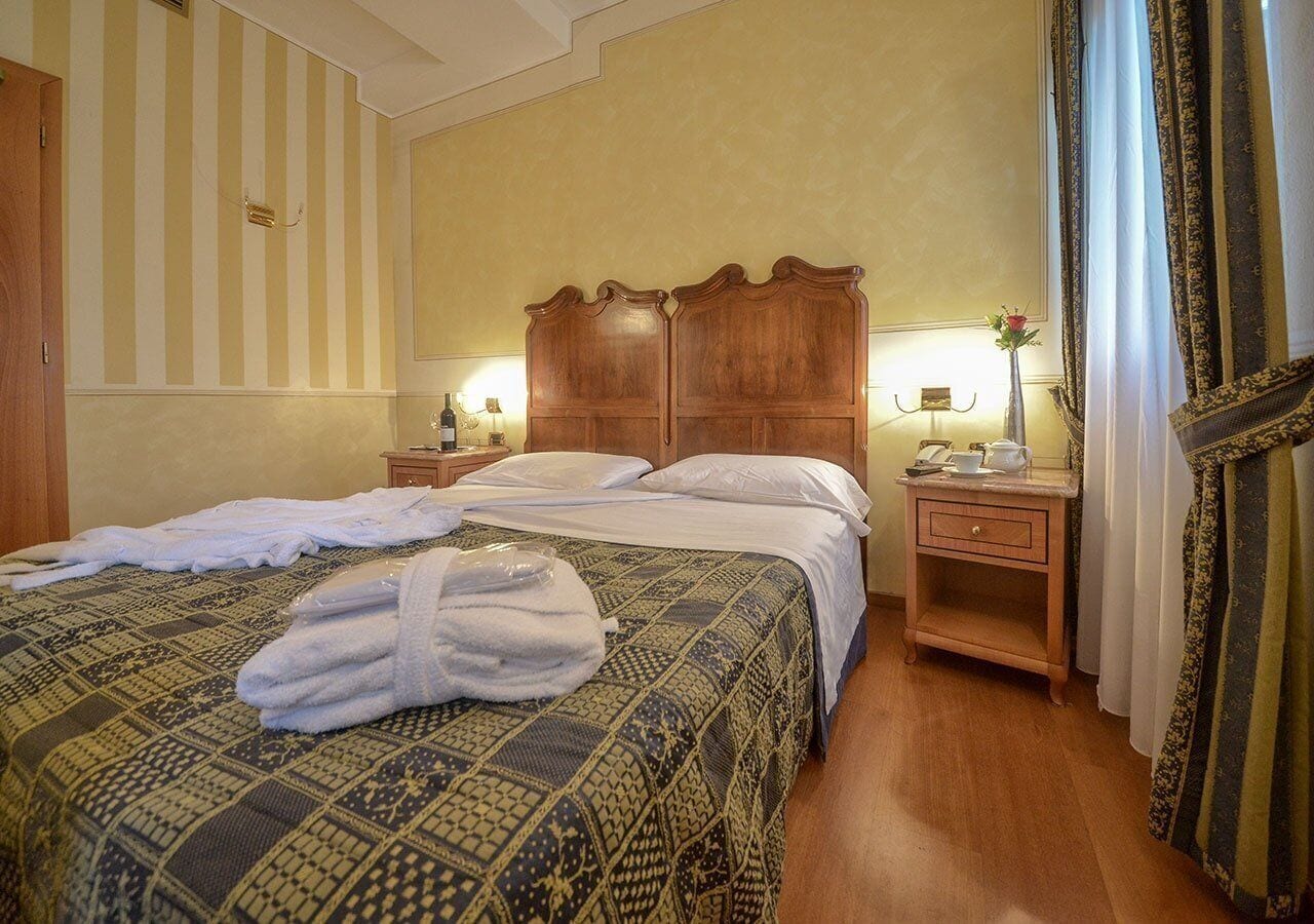 Une chambre d’hôtel comprenant un lit, des tables de chevet, une commode, un miroir et des rideaux.