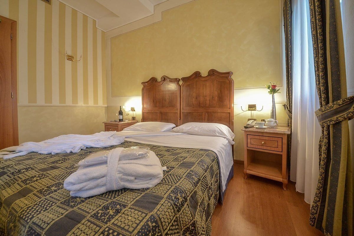 A hotel room with a bed, bedside tables, a nightstand, a mirror, and curtains.