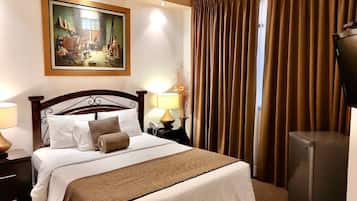 A hotel room with a large bed, a painting on the wall, a desk with a lamp, and a television.