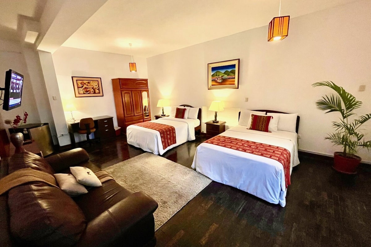 A hotel room with two beds, a sofa, a desk, and a TV.