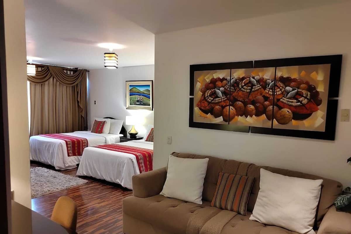 A hotel room with two beds, a sofa, a desk, and a painting on the wall.