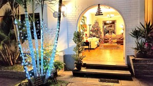 Una entrada cálidamente iluminada con un árbol de Navidad y luces, que conduce a una sala de estar acogedora con un sofá y un árbol de Navidad.