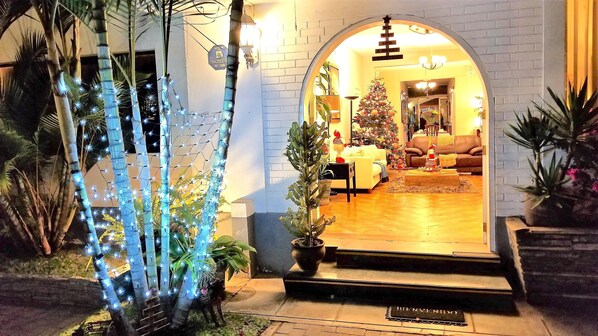 A warmly lit entrance with a Christmas tree and string lights, leading to a cozy living room with a sofa and a Christmas tree. - Casa Bella Boutique Hotel San Isidro (Lima)