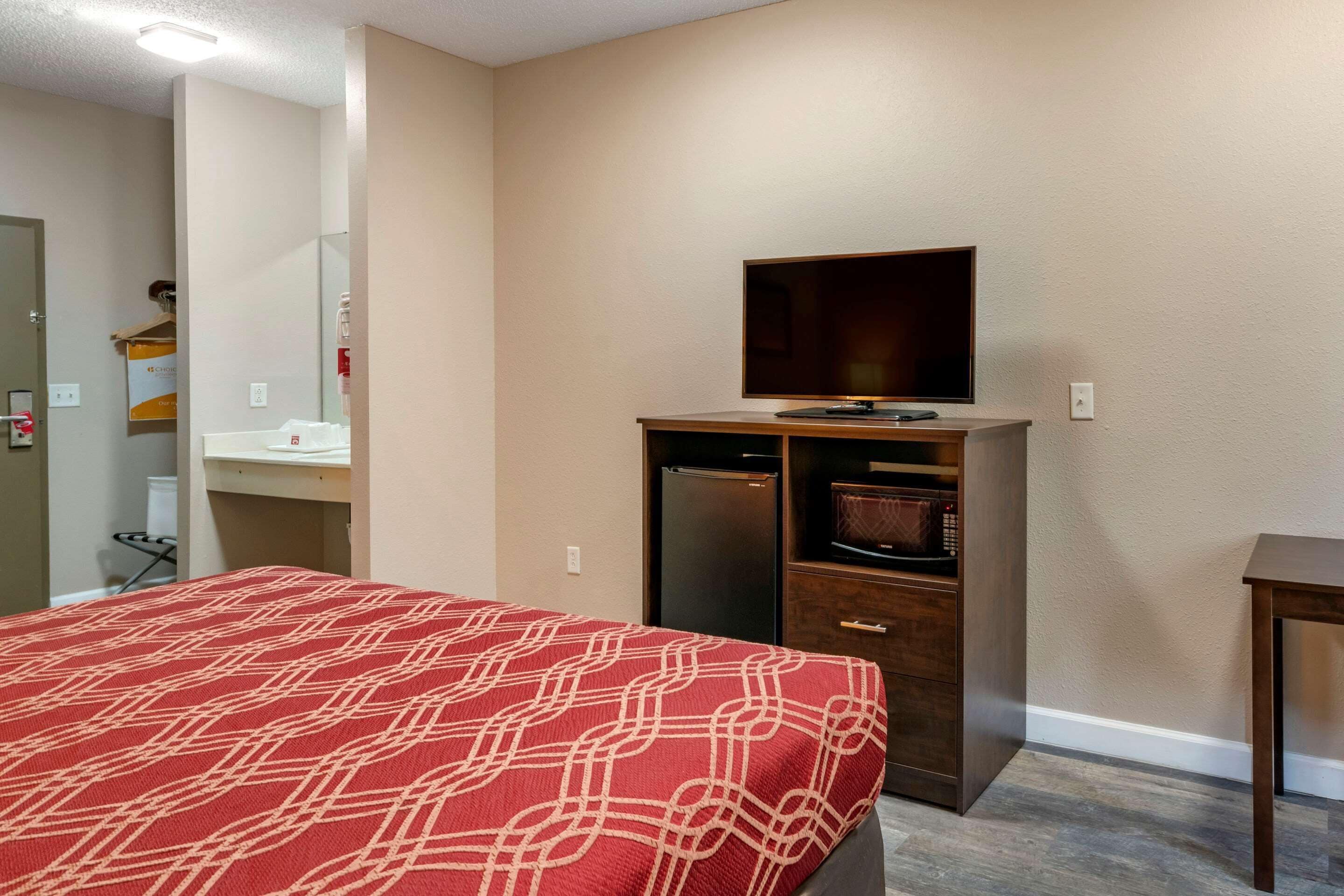 A hotel room with a bed, a television on a wooden stand, a microwave, and a small table.