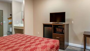 A hotel room with a bed, a television on a wooden stand, a microwave, and a small table.