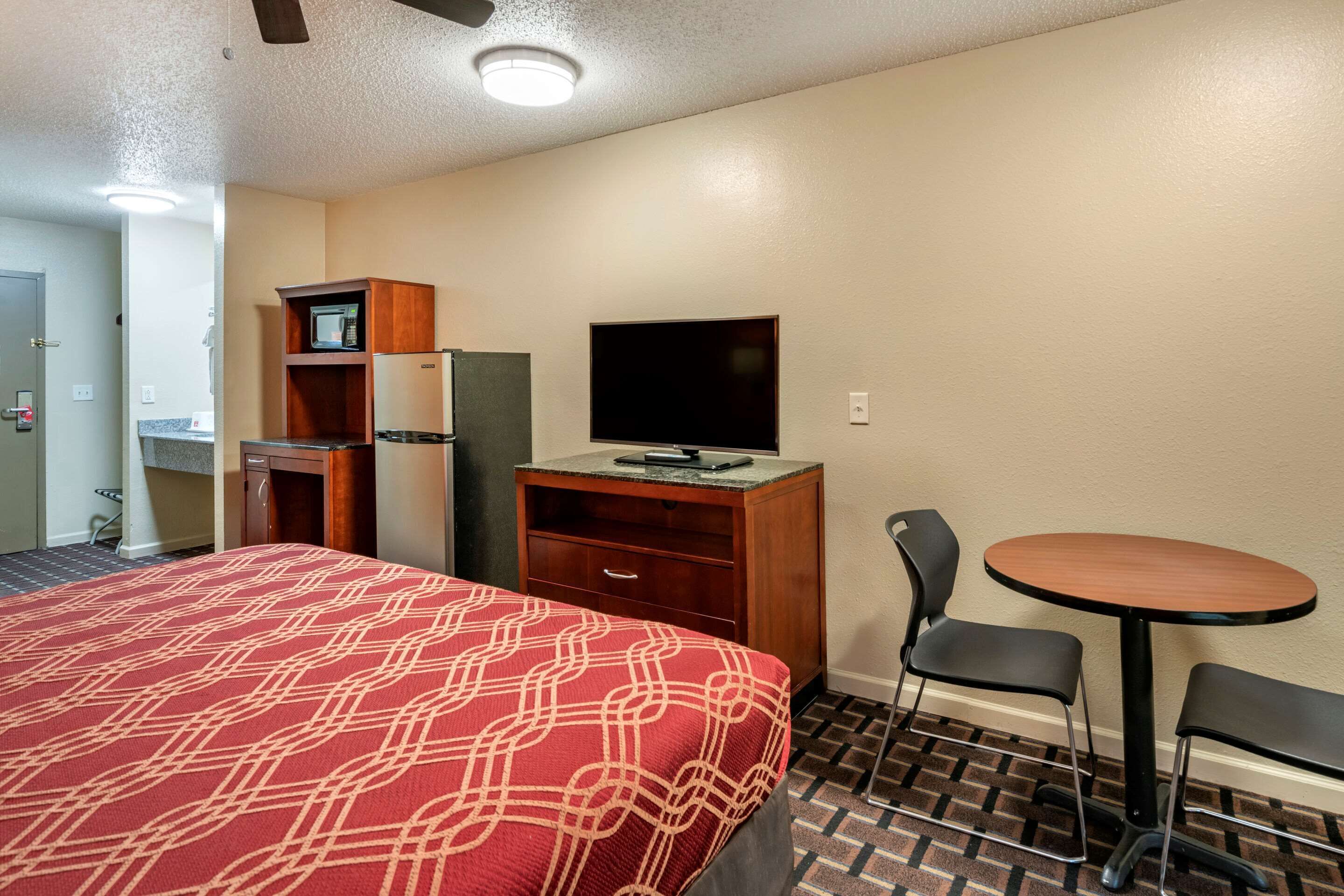 A hotel room with a bed, a desk with a flat-screen TV, a microwave, and a small dining table with two chairs.