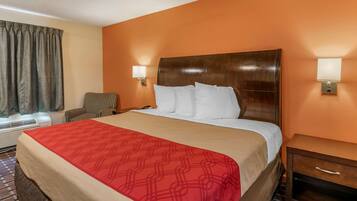 A hotel room with a large bed, a wooden headboard, two bedside lamps, a small table, and a chair.