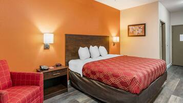 A hotel room with a large bed, a red armchair, a nightstand with a phone and a lamp, and a map on the wall.
