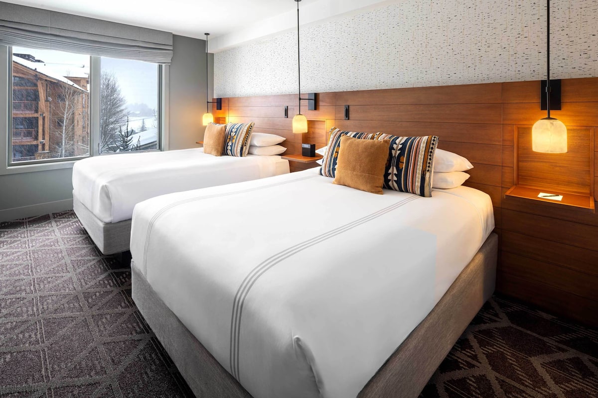 A hotel room with two beds, a large window, and a patterned wall.