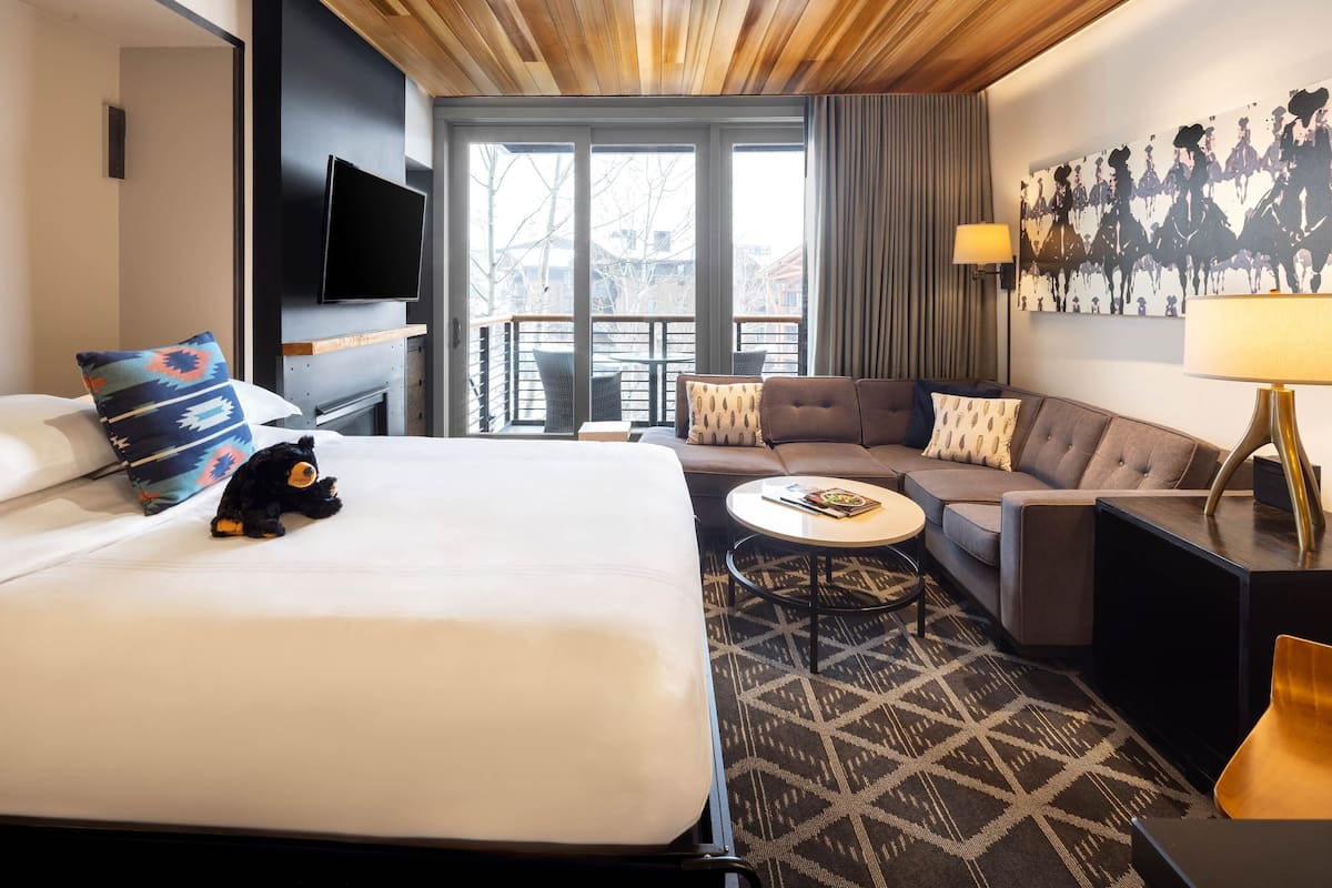 A hotel room with a large bed, a sofa, a small coffee table, a TV, and a balcony with a view.
