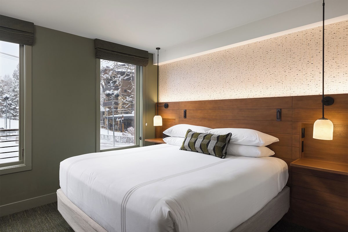 A hotel room with a large bed, wooden headboard, and a view of the outdoors.