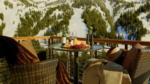 Ein Tisch mit einer Weinflasche, Gläsern, Käse und Trauben auf einem Balkon mit Blick auf die Berge.