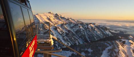 A cable car with a red and black design, suspended over a snowy mountain landscape with clear skies.