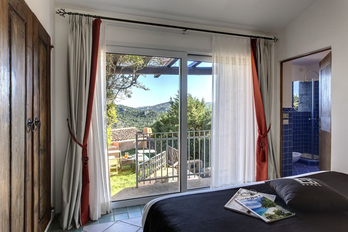 A bedroom with a bed, a magazine, and a view of a balcony with outdoor furniture.