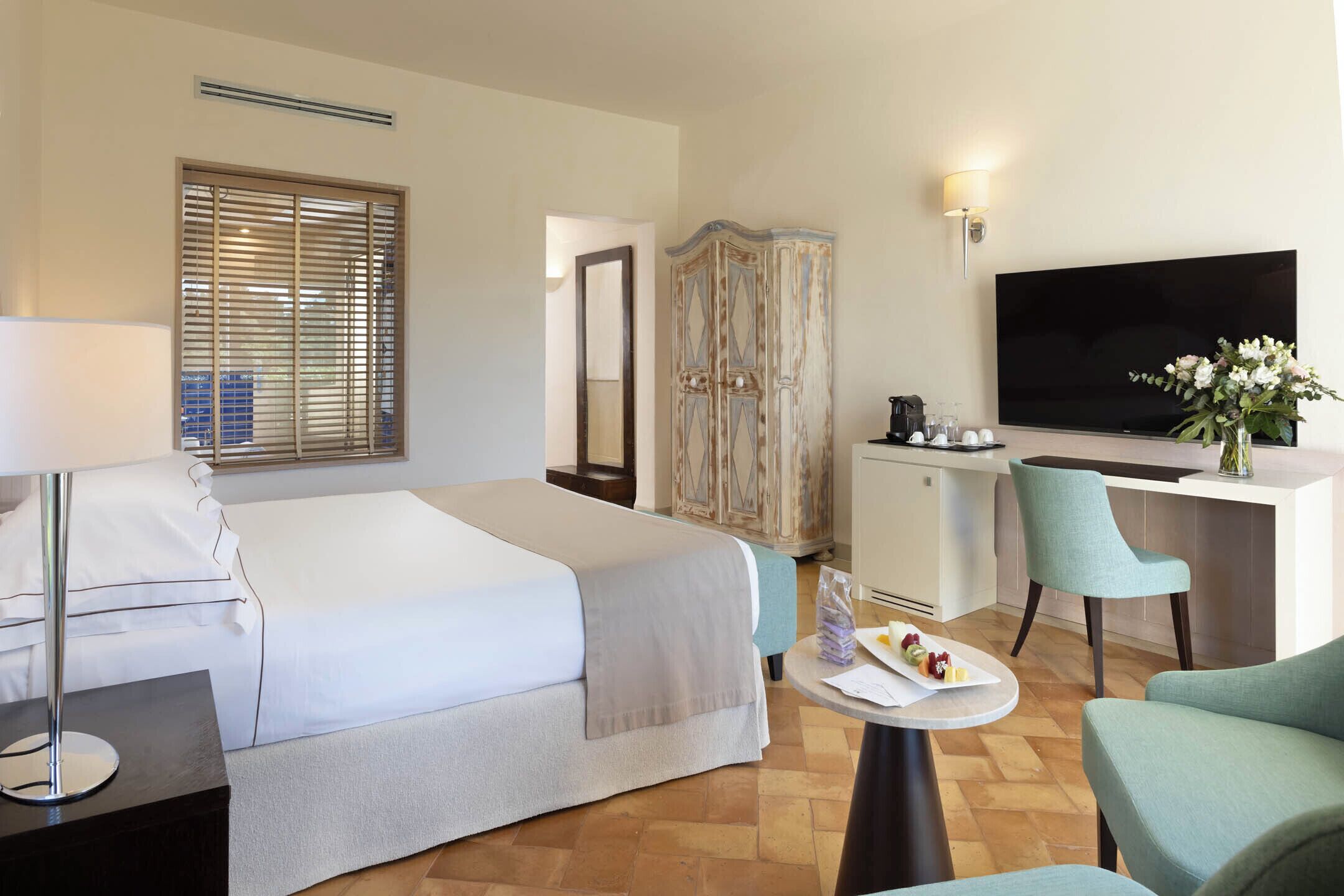 A hotel room with a bed, desk, TV, and seating area.