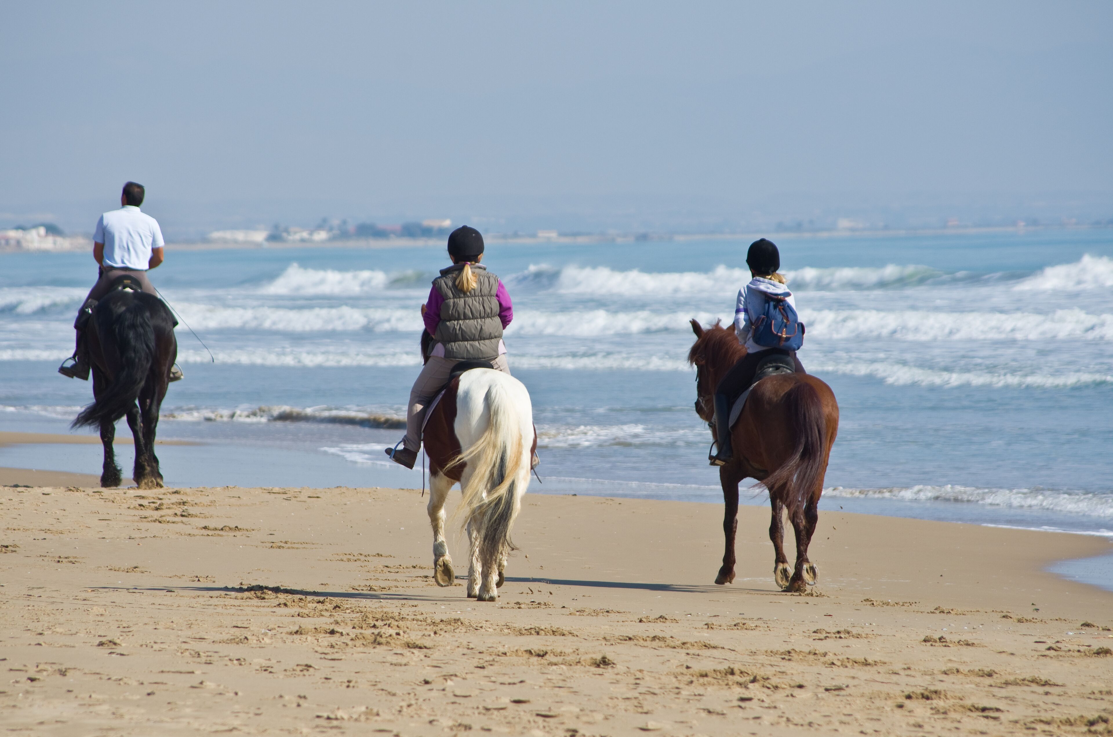 Three people riding horses on a beach with the ocean in the background.