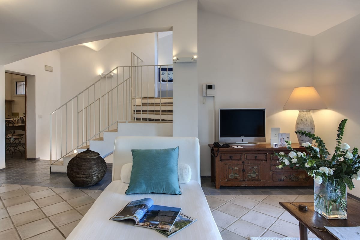 A modern living room with a sofa, a coffee table with magazines, a TV, a lamp, and a staircase leading to another room.