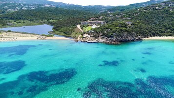 Zona costera con aguas turquesas cristalinas, una playa de arena y un complejo arquitectónico rodeado de vegetación.