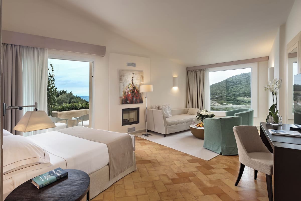 A hotel room with two beds, a sofa, a desk, and a view of the outdoors.